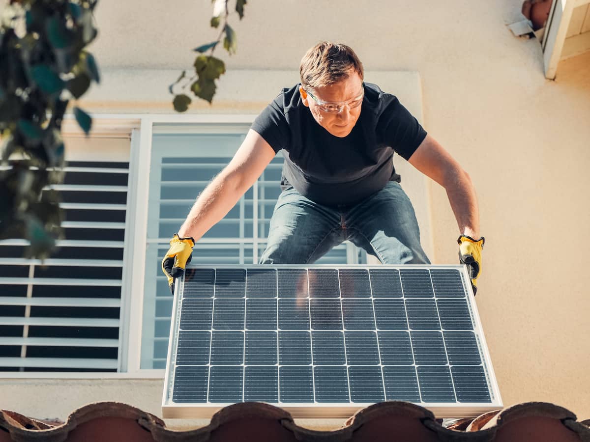 un tehnician monteaza panouri fotovoltaice pe acoperisul unei cladiri